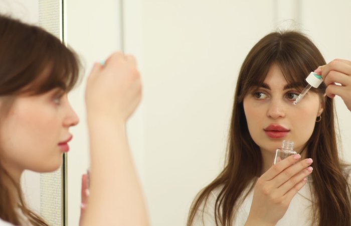 A young woman applying skincare serum in front of a mirror indoors. Perfect for beauty and self-care themes.